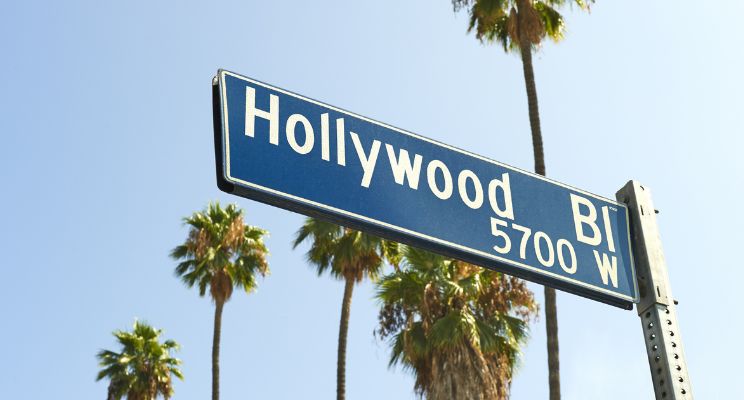 close up from below of Hollywood Blvd street sign against palm trees and blue sky background