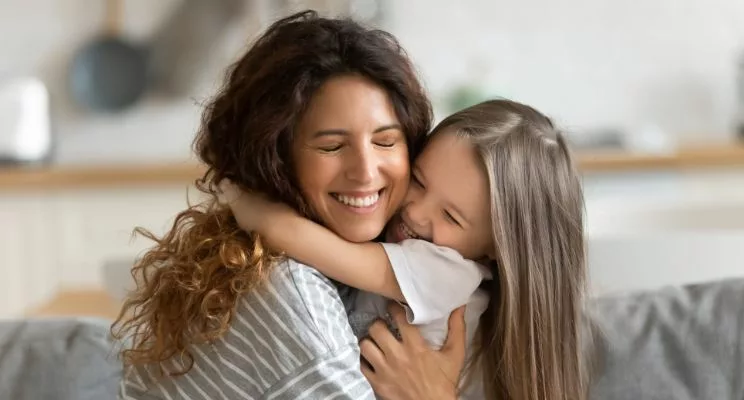 Smiling woman hugging happy daughter.