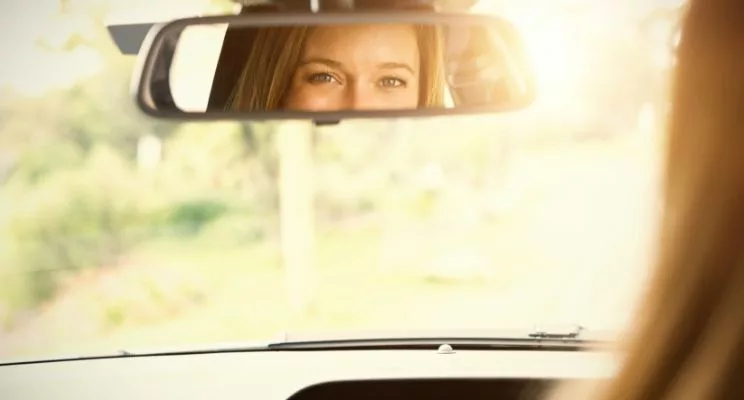 woman looking in rear view mirror of car